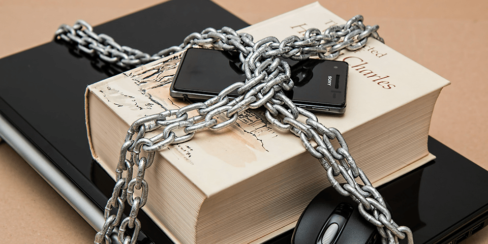 A book, phone, laptop, and computer mouse, chained together