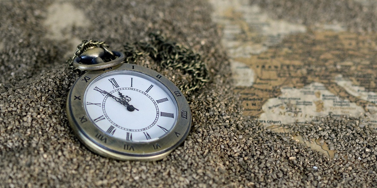 A pocket watch sits in a bed of sand on top of a world map