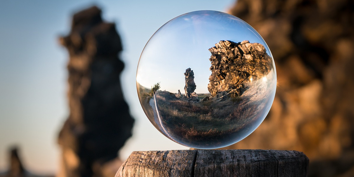 A glass sphere balanced on a wooden post, the area outside of the sphere is out of focus, but the sphere itself gives perfect focused detail of the landscape behind.